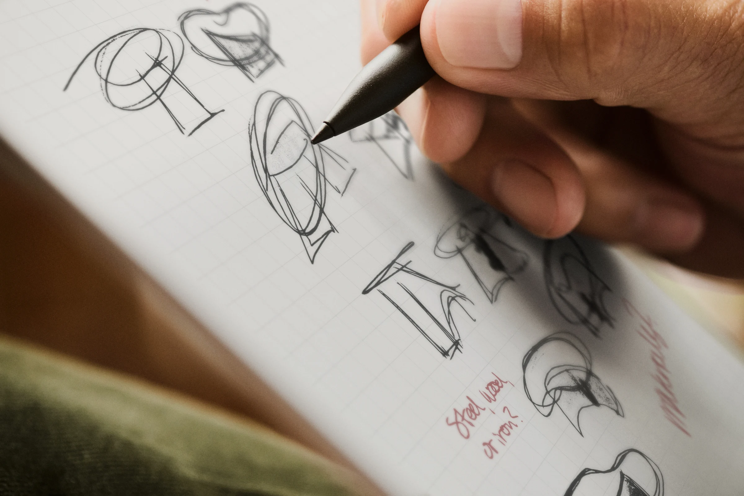 Macro view of a designer's hand using a Marker Plus to draw multiple geometric concept sketches on a grid-lined reMarkable paper tablet.
