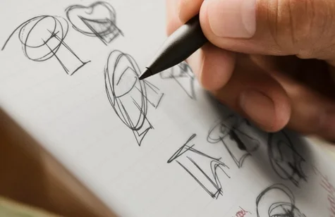 Macro view of a designer's hand using a Marker Plus to draw multiple geometric concept sketches on a grid-lined reMarkable paper tablet.
