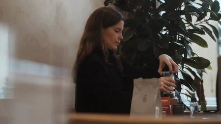 Woman next to a plant making a cup of coffee.
