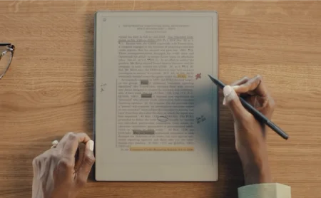 A reMarkable paper tablet showing a document with highlighted text and markups, a hand is writing with the Marker.