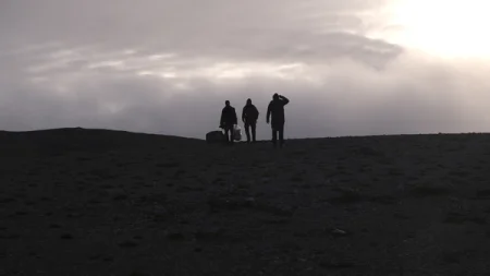 Silhouetted figures walk across a landscape under a cloudy sky.