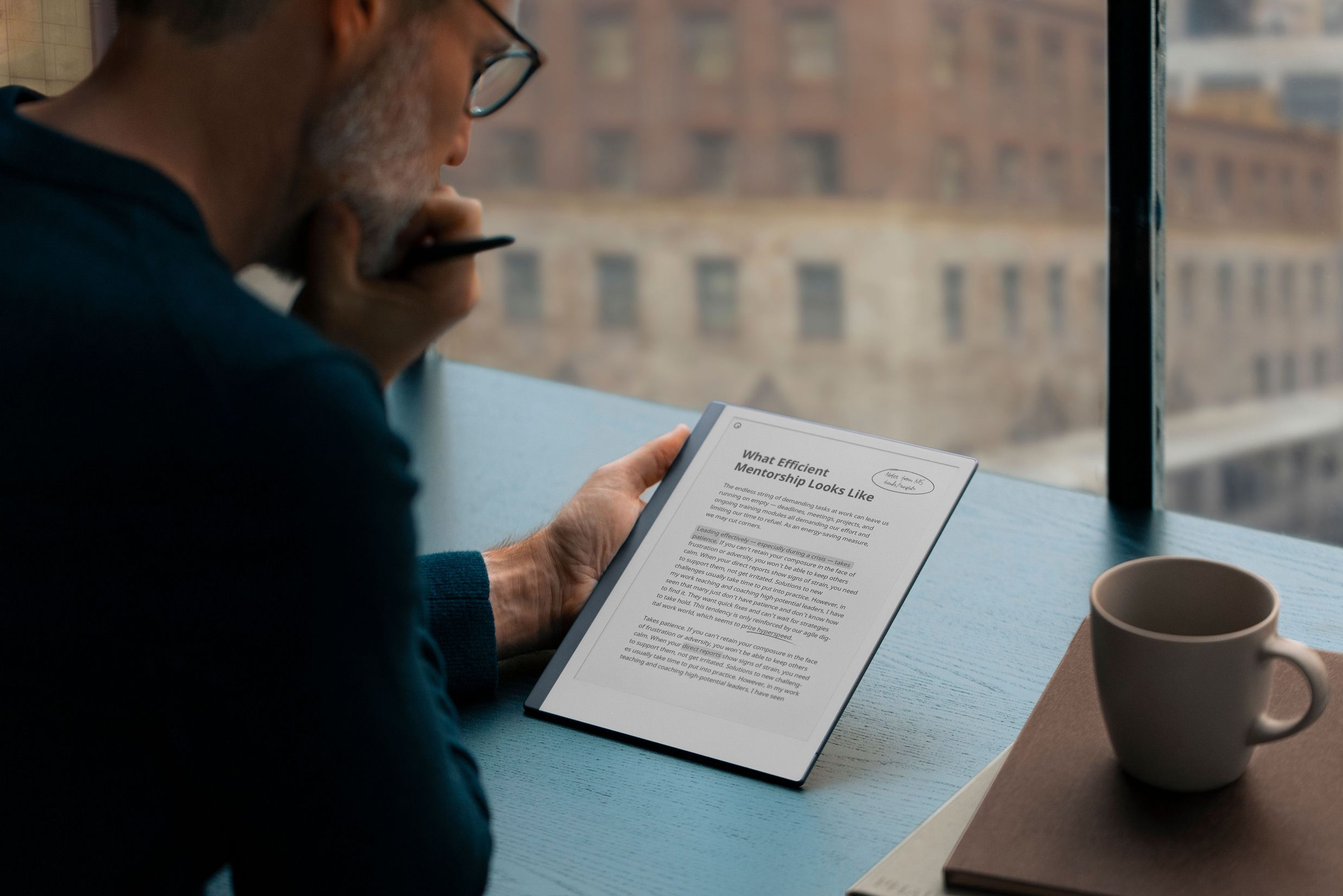 A reMarkable paper tablet displaying text with a man holding a Marker near a window.

