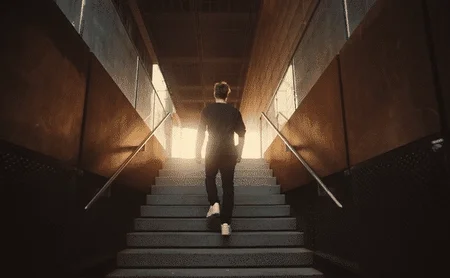 A man walks up a staircase toward light.