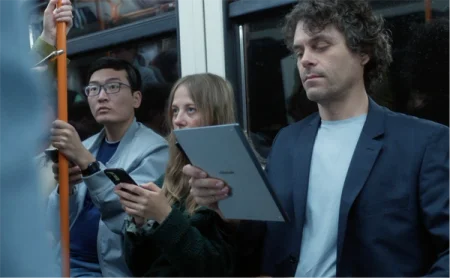 A man holds the reMarkable paper tablet on a train, near two others on their phones.