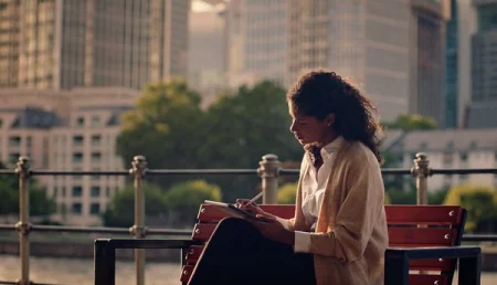 Woman writing on her reMarkable paper tablet with the Marker, sitting on a park bench.