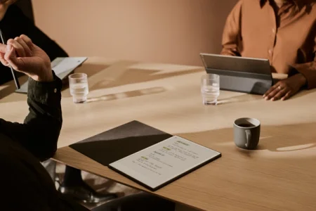A reMarkable paper tablet displaying notes in a meeting, next to coffee and water glasses.