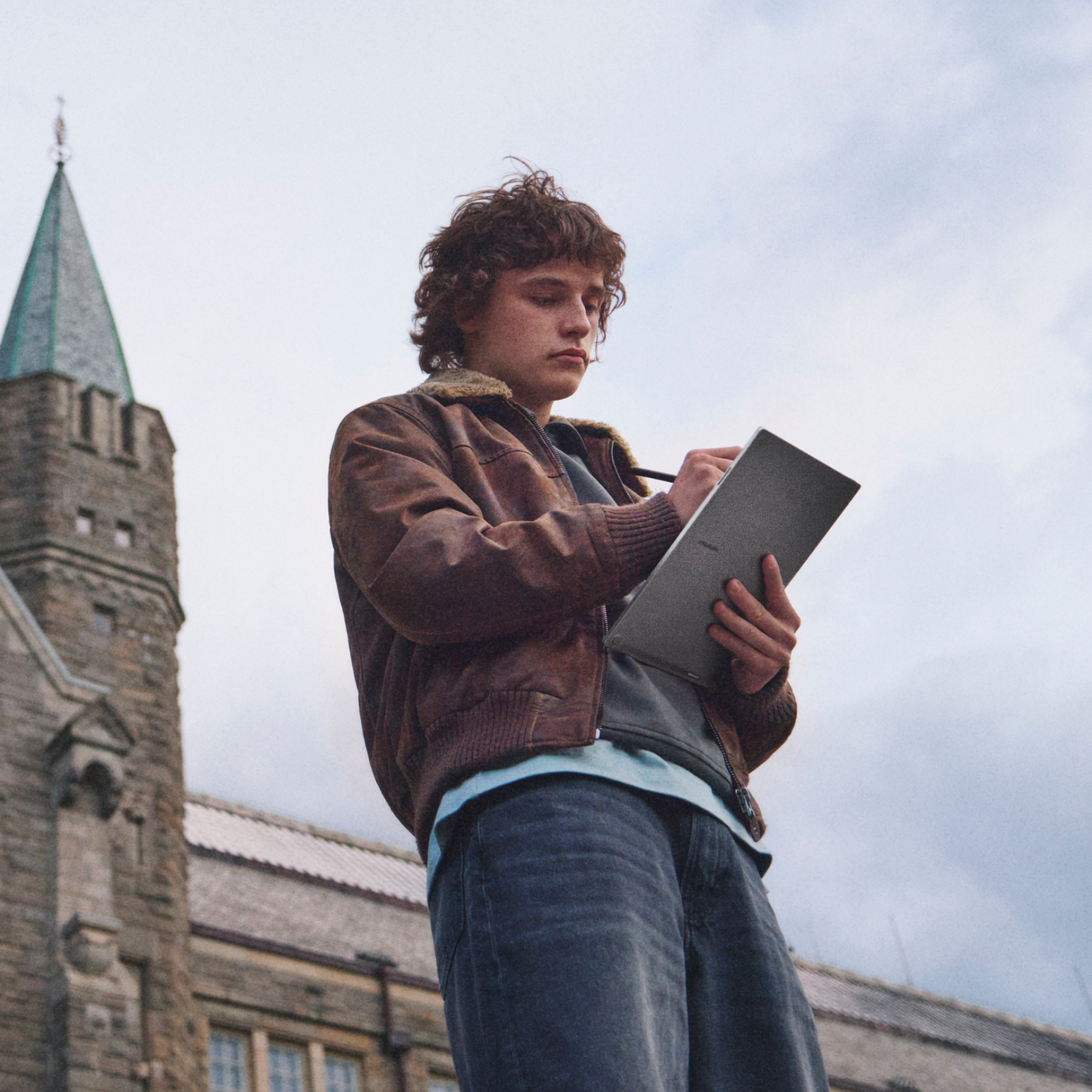A student standing outside, writing a note on the reMarkable Paper Pro.