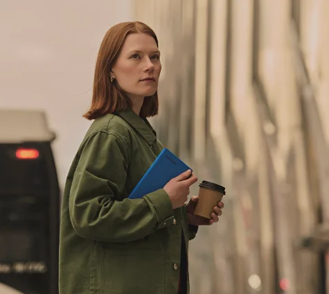 Woman holding reMarkable Paper Pro Move tablet with a Book Folio cover and coffee cup in city.