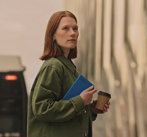 Person outside holding a reMarkable Paper Pro Move tablet with a Book Folio in one hand and a coffee in the other hand.