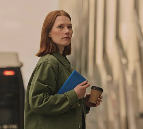 Person outside holding a reMarkable Paper Pro Move tablet with a Book Folio in one hand and a coffee in the other hand.