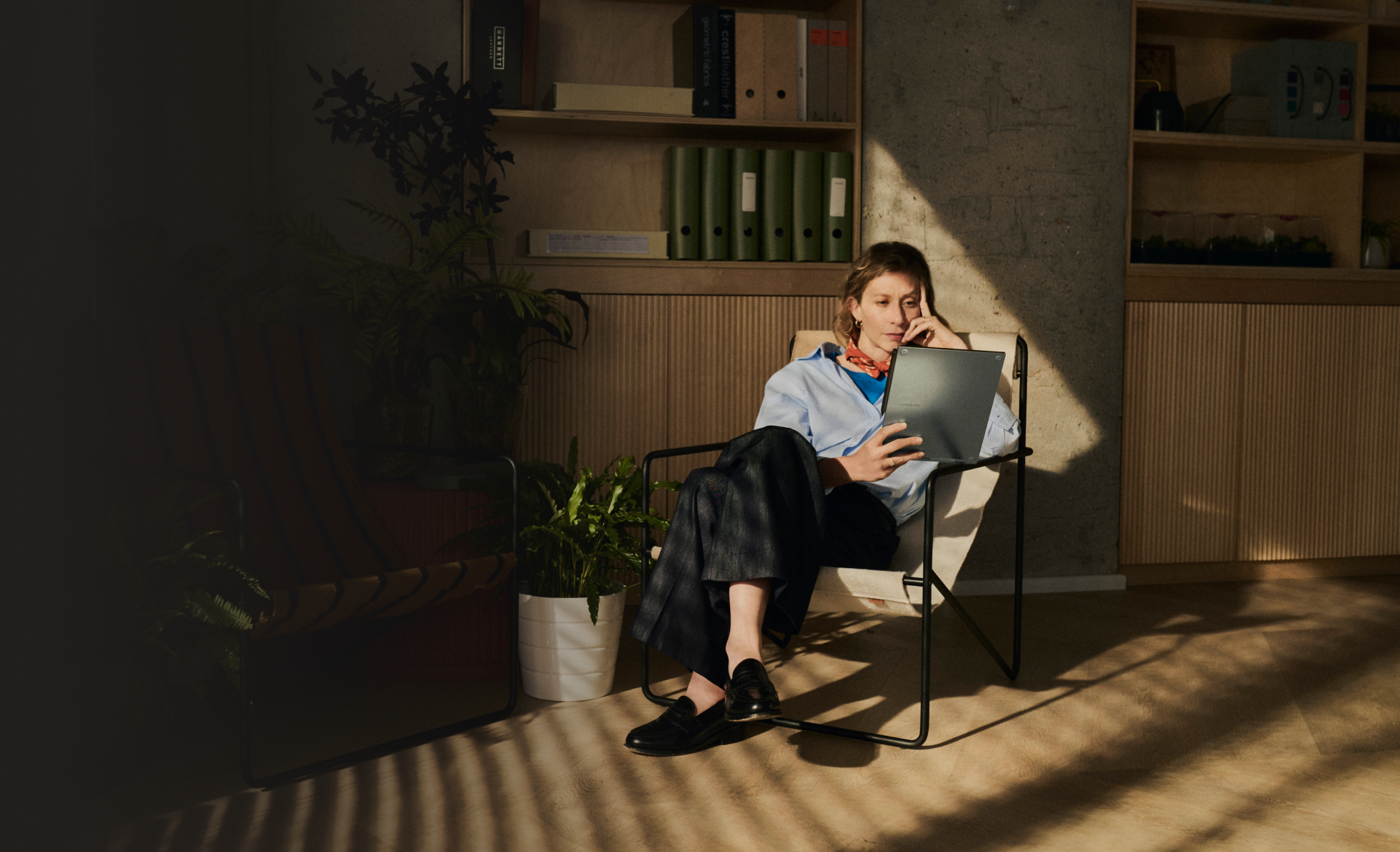 A woman sits in a chair looking at the reMarkable paper tablet.
