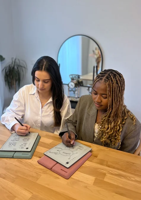 Hazal Trench and Lydie Kitenge sitting at a table, each writing on their own reMarkable Paper Pure tablet.