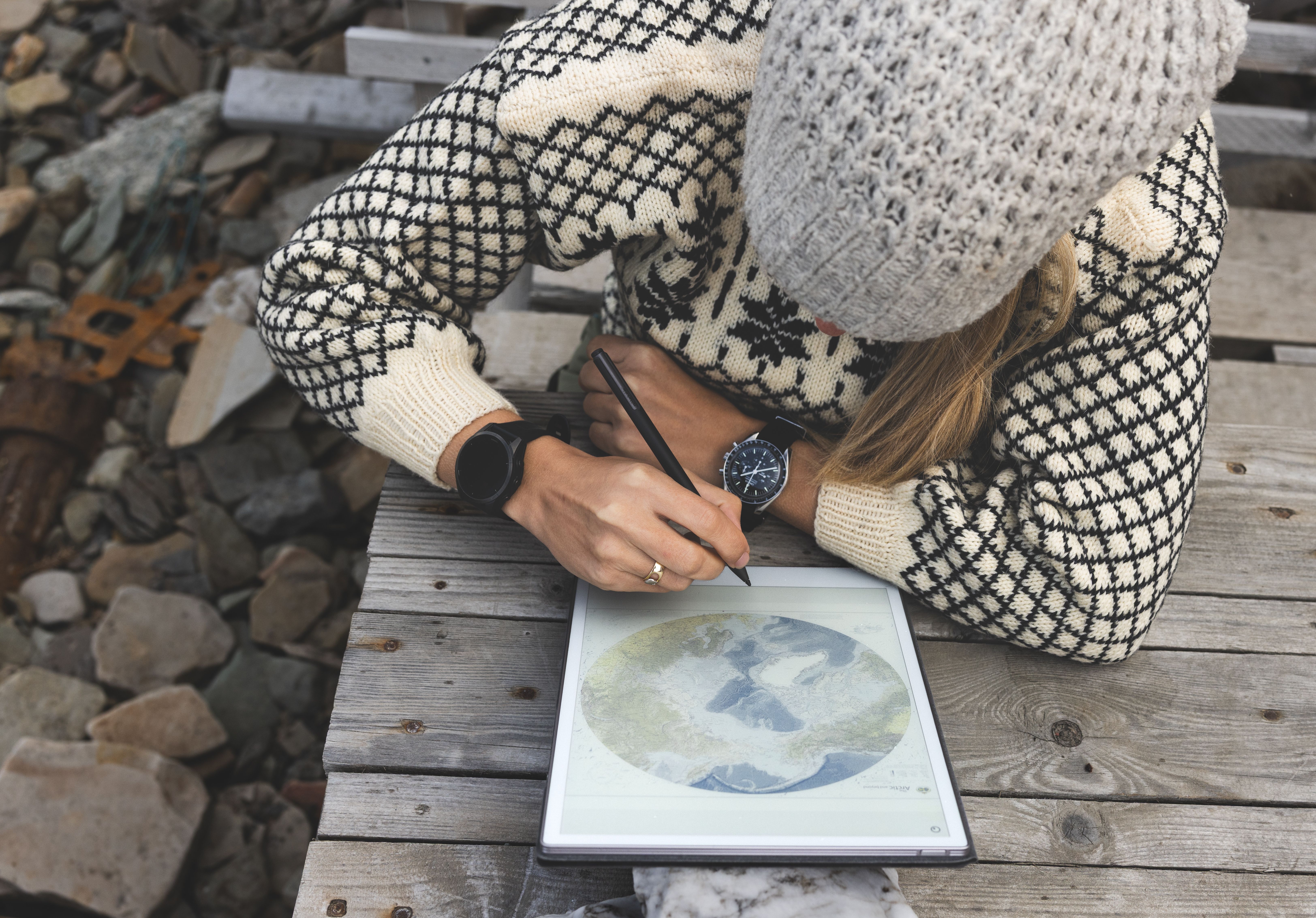 A reMarkable paper tablet showing a map, with Jannicke Mikkelsen drawing with the Marker on a wooden table.
