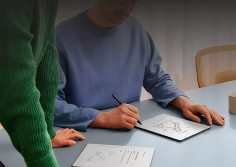 A man at a table writing on a reMarkable Paper tablet, in discussion with a woman looking at his notes