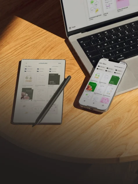 reMarkable paper tablet and Marker with laptop and phone on a wood table showing digital files.