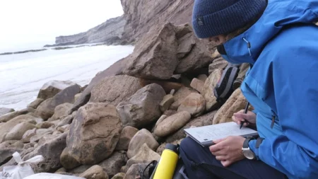 A person writing on the reMarkable paper tablet with the Marker on a rocky beach.