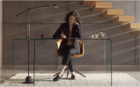 A woman writing at a glass desk.
