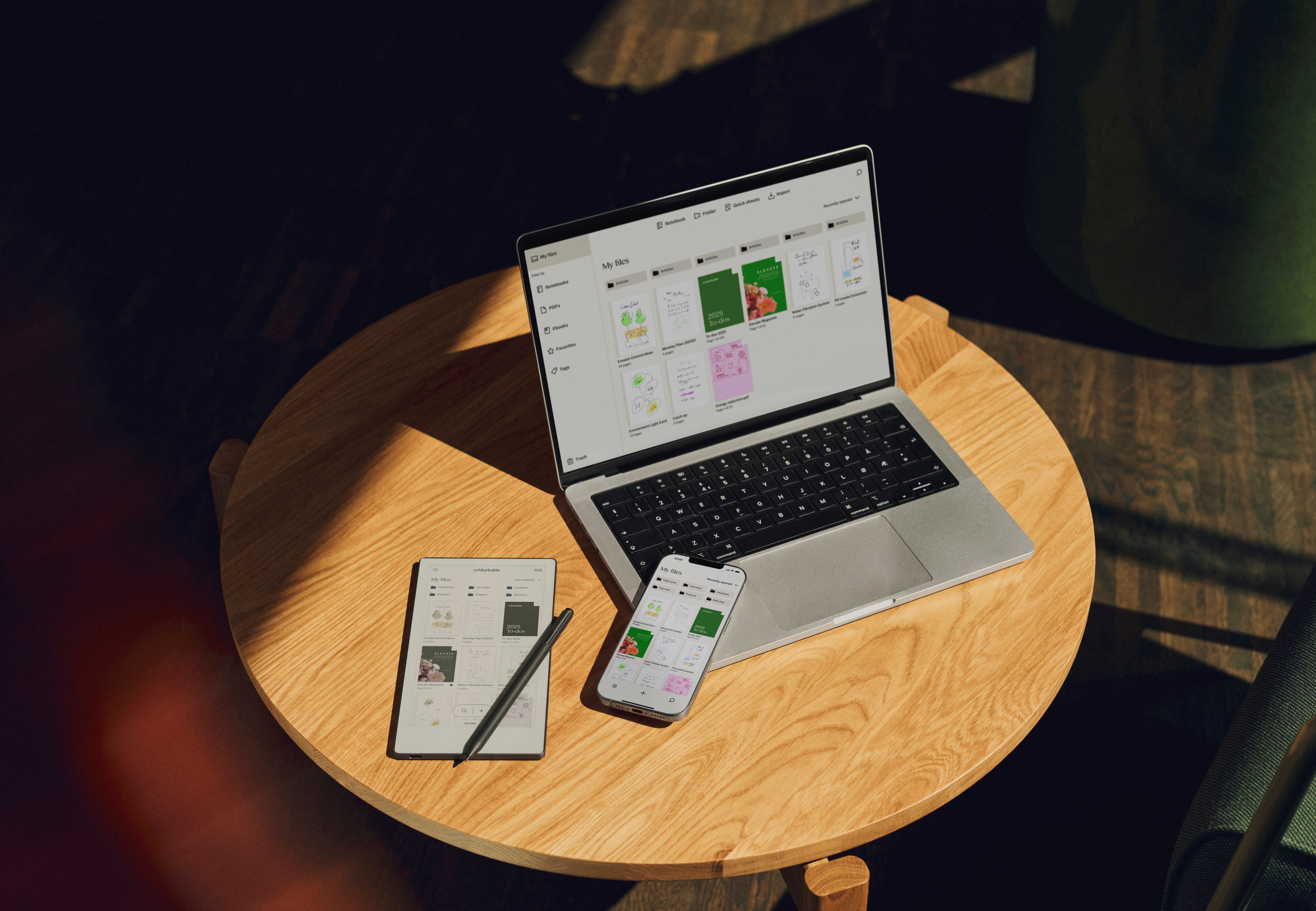 A reMarkable Paper Pro Move with Marker Plus laying on a coffee table next to a laptop and phone, all displaying the same synced content.