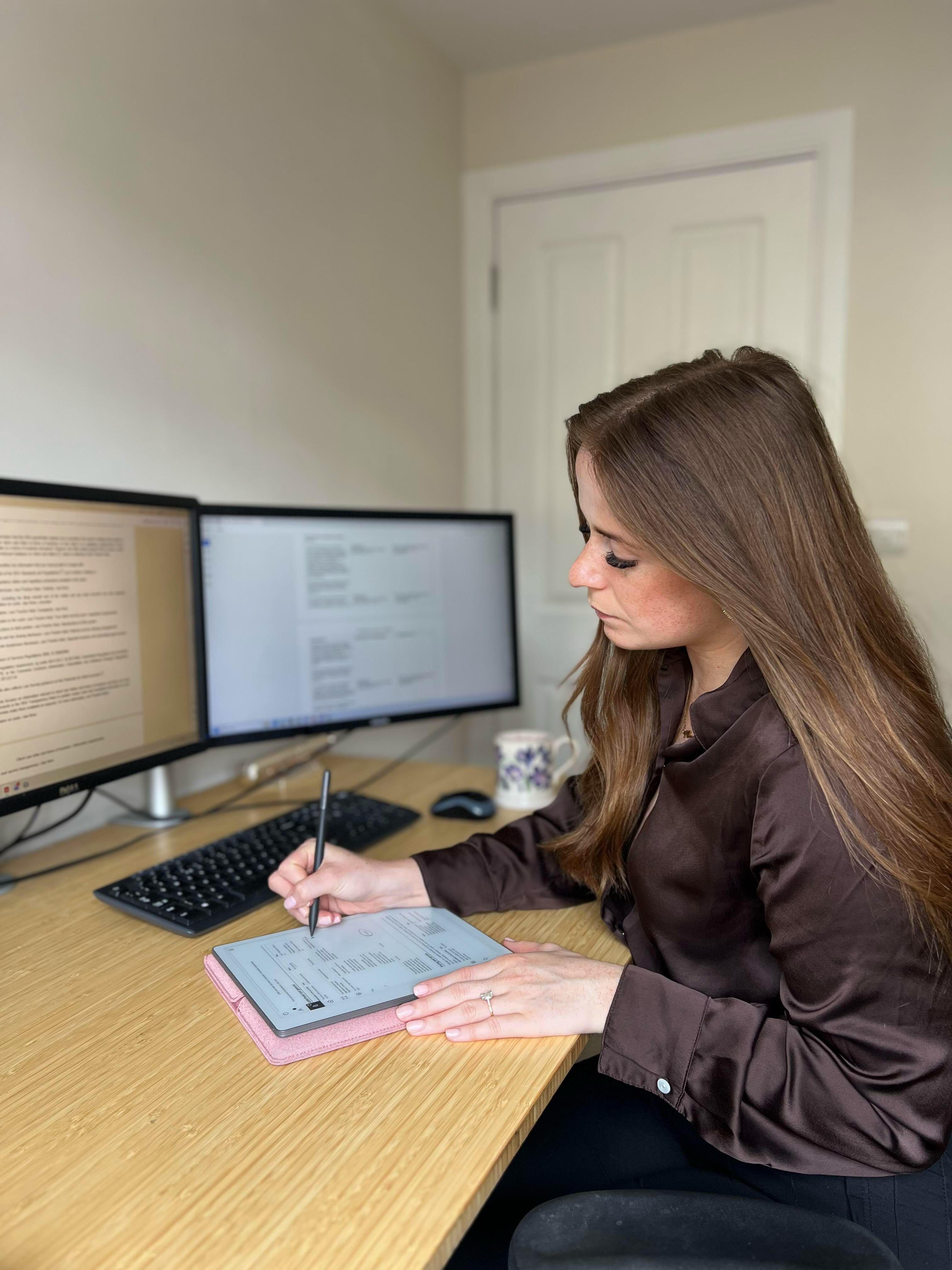 Mia Siddique sitting down at a desk writing on her reMarkable Paper Pure. 