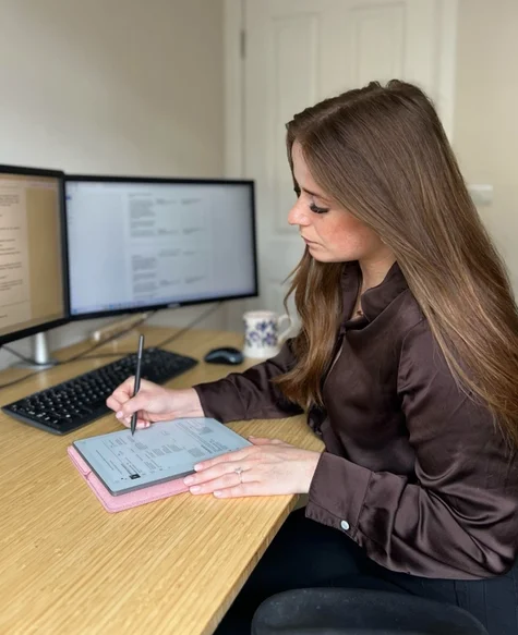 Mia Siddique sitting down at a desk writing on her reMarkable Paper Pure.