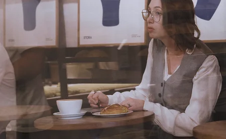 Sian sits at a table with a pastry and coffee.