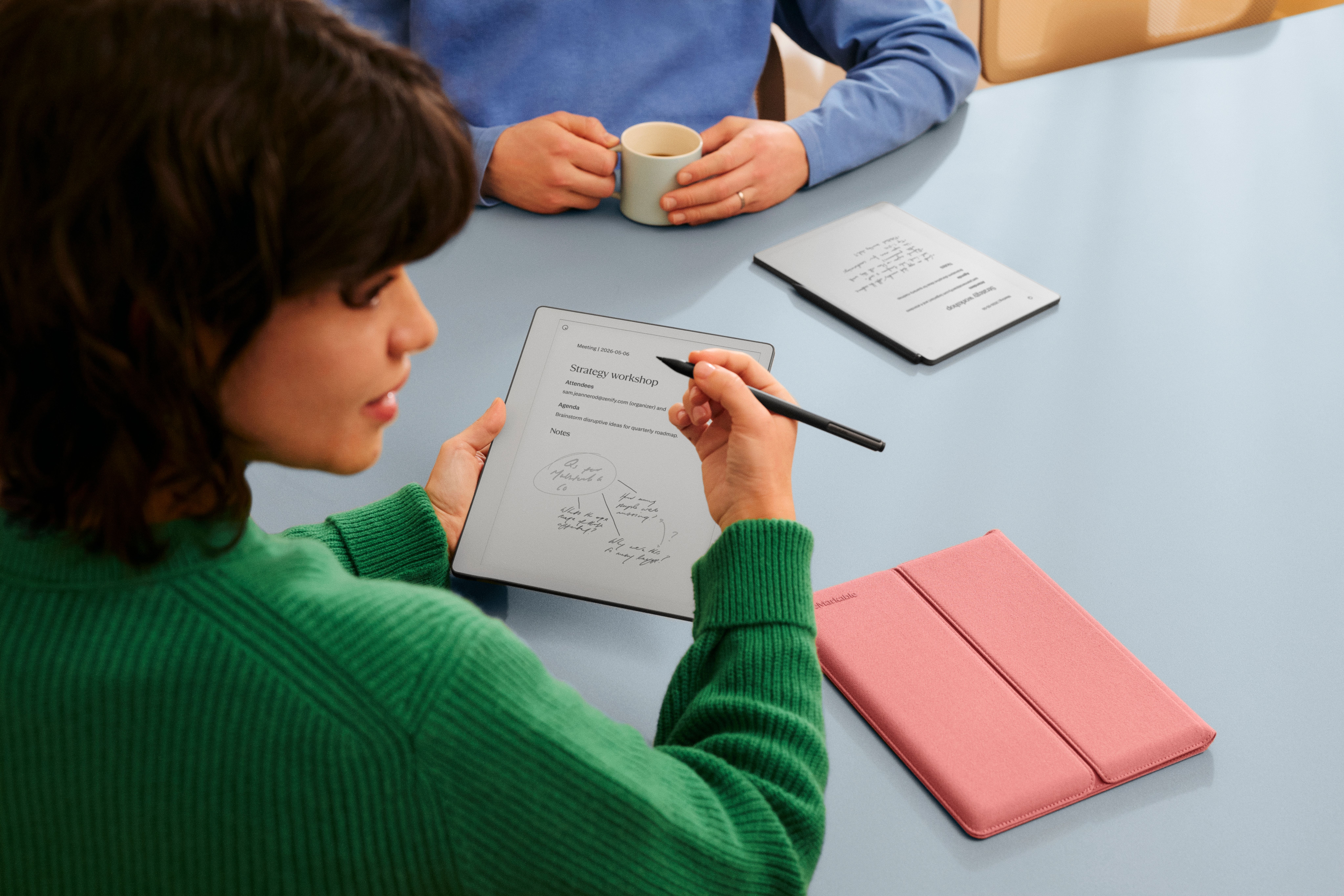A woman and man in a meeting room sit in discussion while making notes on their reMarkable Paper Pure tablets