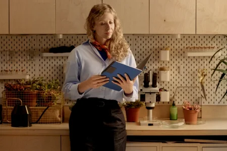 A woman holding a reMarkable in a blue Book Folio in a workspace with plants and a microscope.