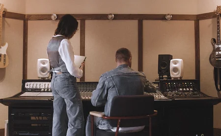 Two people working at a recording studio with mixing equipment and monitors.