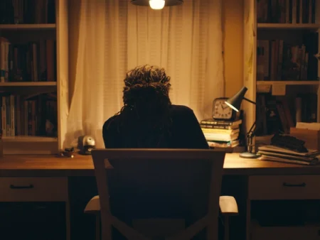 A person at a desk with books and a lamp.