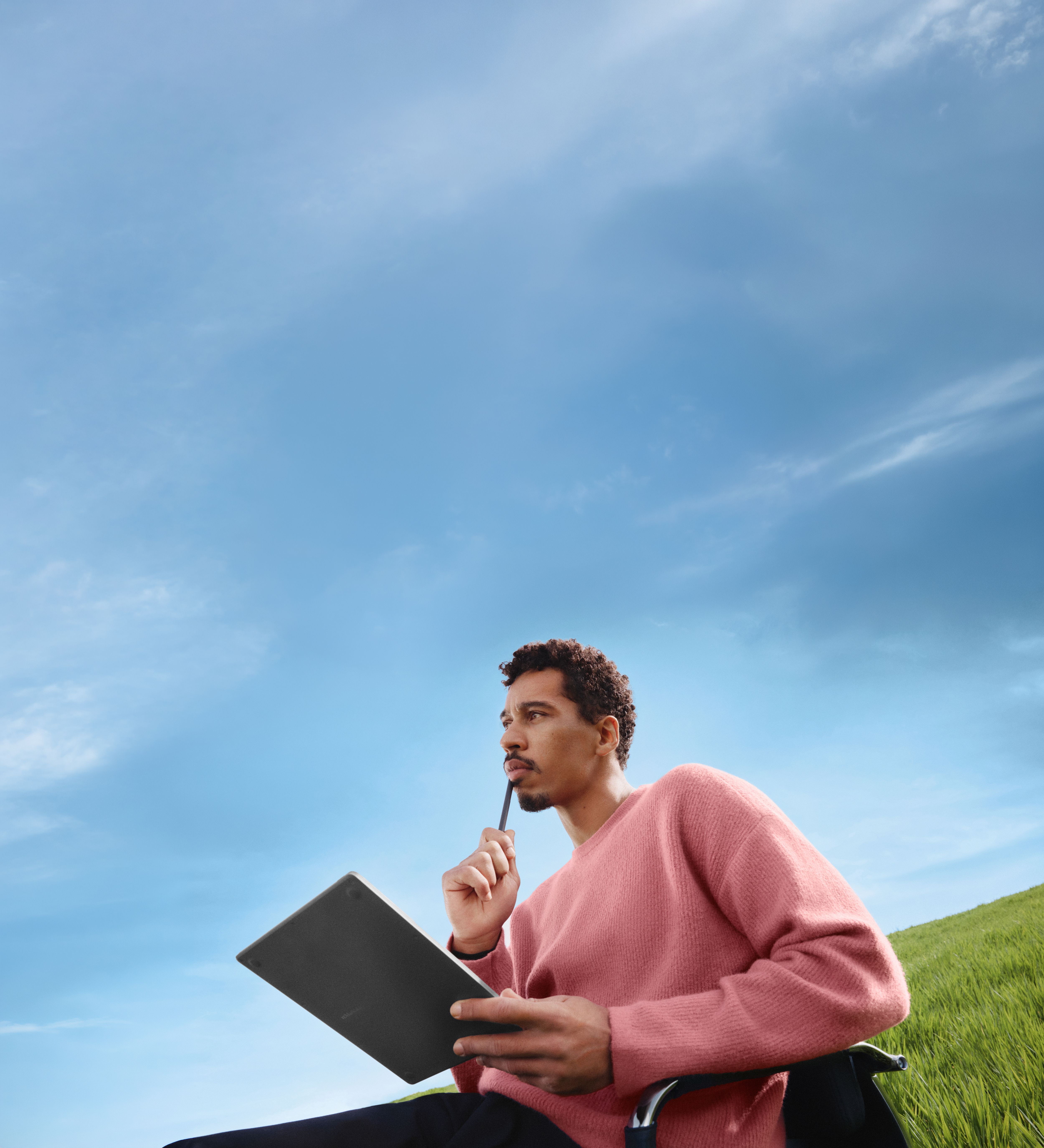 A man sitting on an office chair in a green field with blue sky, thinking with his reMarkable Paper Pure