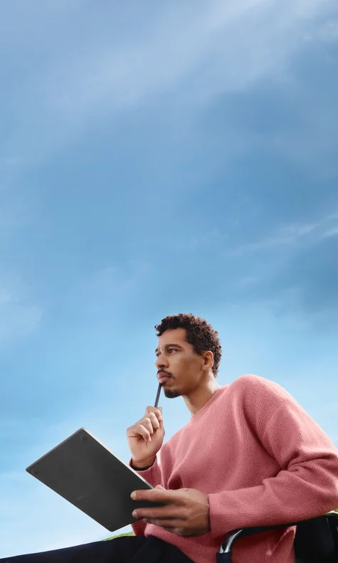 A man sitting on an office chair in a green field with blue sky, thinking with his reMarkable Paper Pure