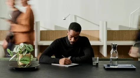 A man sitting at a table writing a note on a reMarkable Paper Pro.
