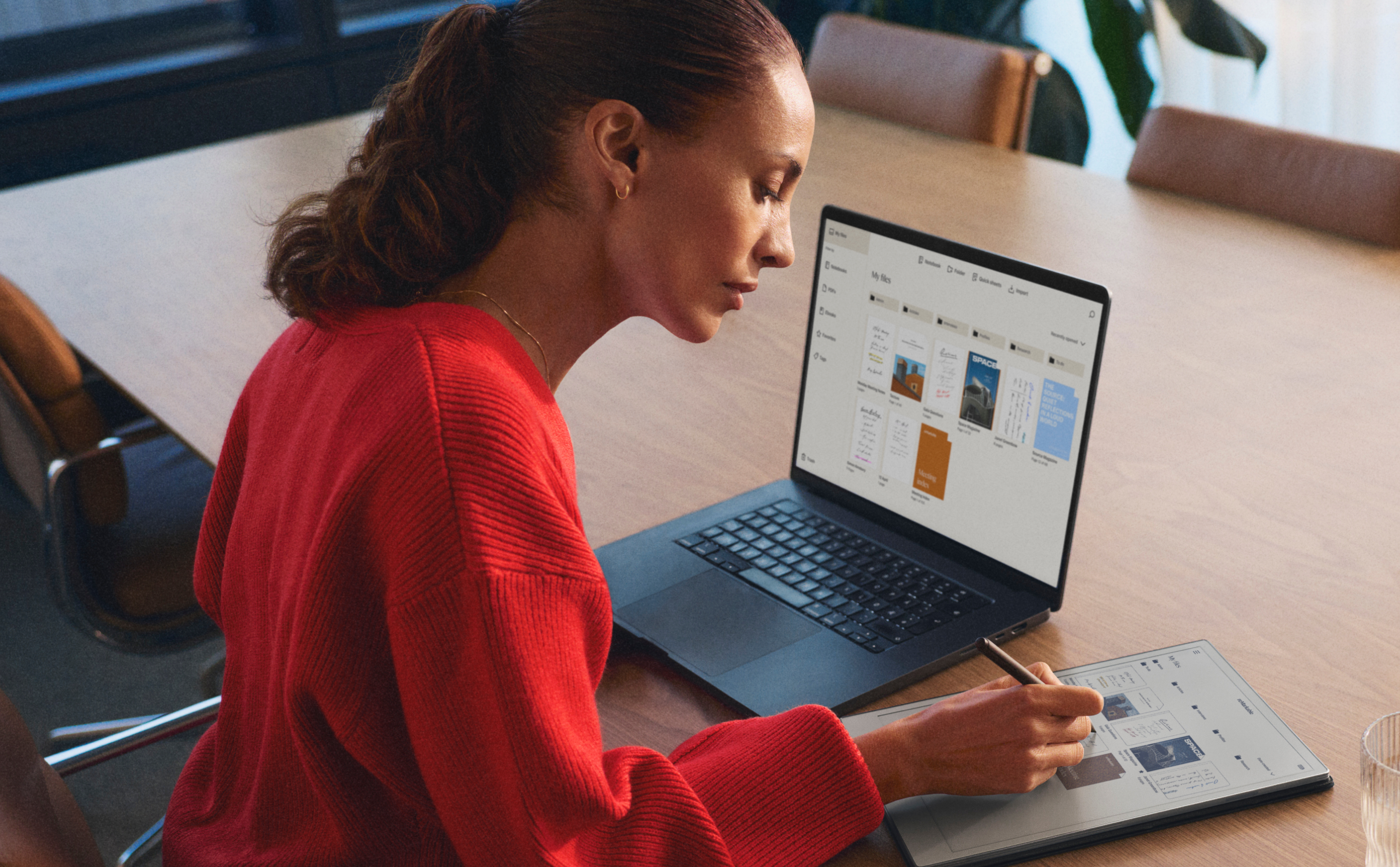 A woman works on a reMarkable Paper Pro, writing with the Marker, alongside an open laptop.