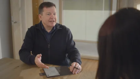 A man discussing notes on a reMarkable paper tablet with the Marker on a wooden table.