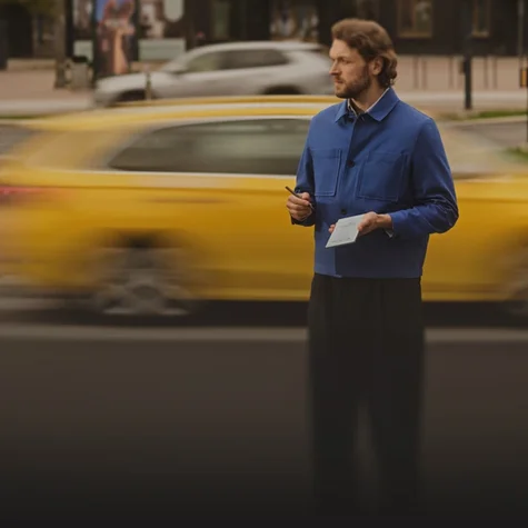 A man standing on a street corner holding a reMarkable Paper Pro Move paper tablet, with traffic moving behind him.