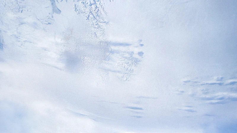 A polar region of the earth as seen from space, with snowy mountains and cloud cover.