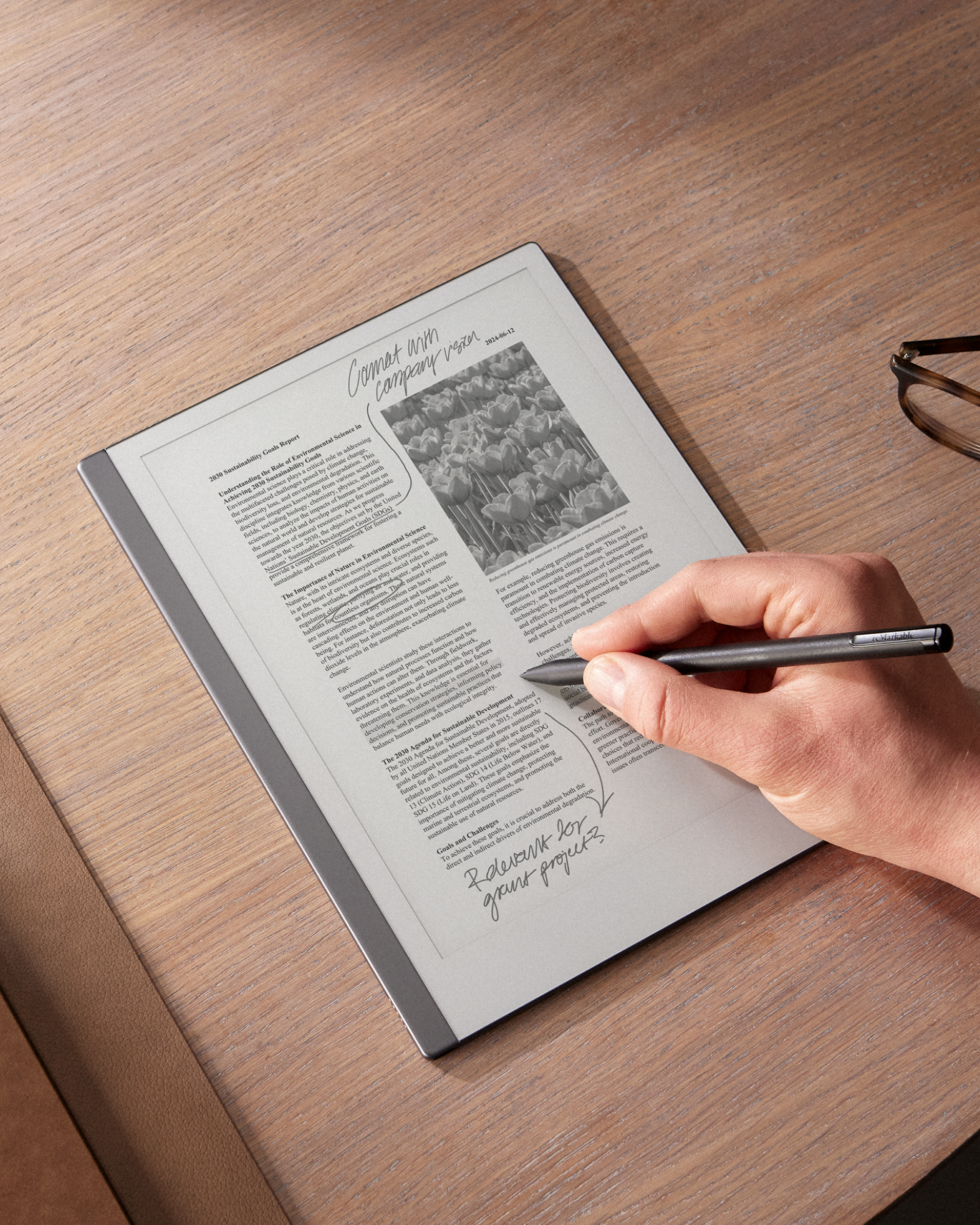 Die Hand einer Person schreibt mit dem Marker Plus auf einem reMarkable 2, das auf einem Holztisch liegt.