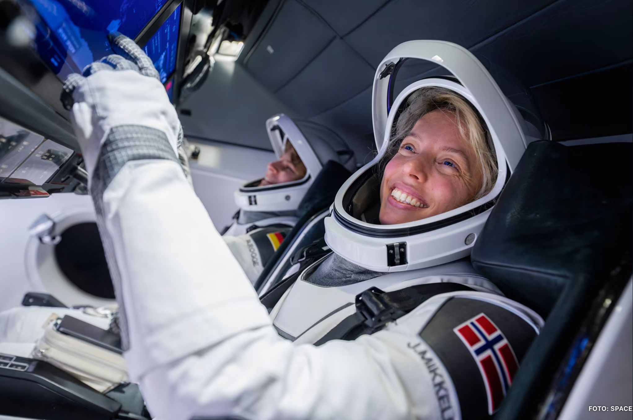 Jannicke Mikkelsen in a spacecraft cabin wearing a spacesuit with the Norwegian flag.