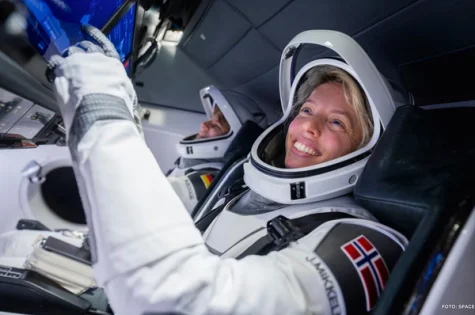 Jannicke Mikkelsen in a spacecraft cabin wearing a spacesuit with the Norwegian flag.
