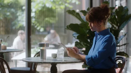 Person using a reMarkable paper tablet at a cafe. The device is visible on the marble table next to a lamp and a glass of water.