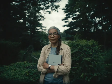 A person holding reMarkable paper tablet in front of lush greenery, wearing glasses and a tan jacket.