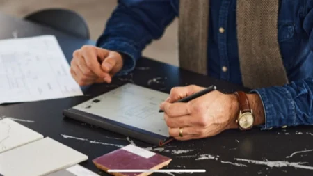 A reMarkable paper tablet on a desk, with someone writing on the device using the Marker.