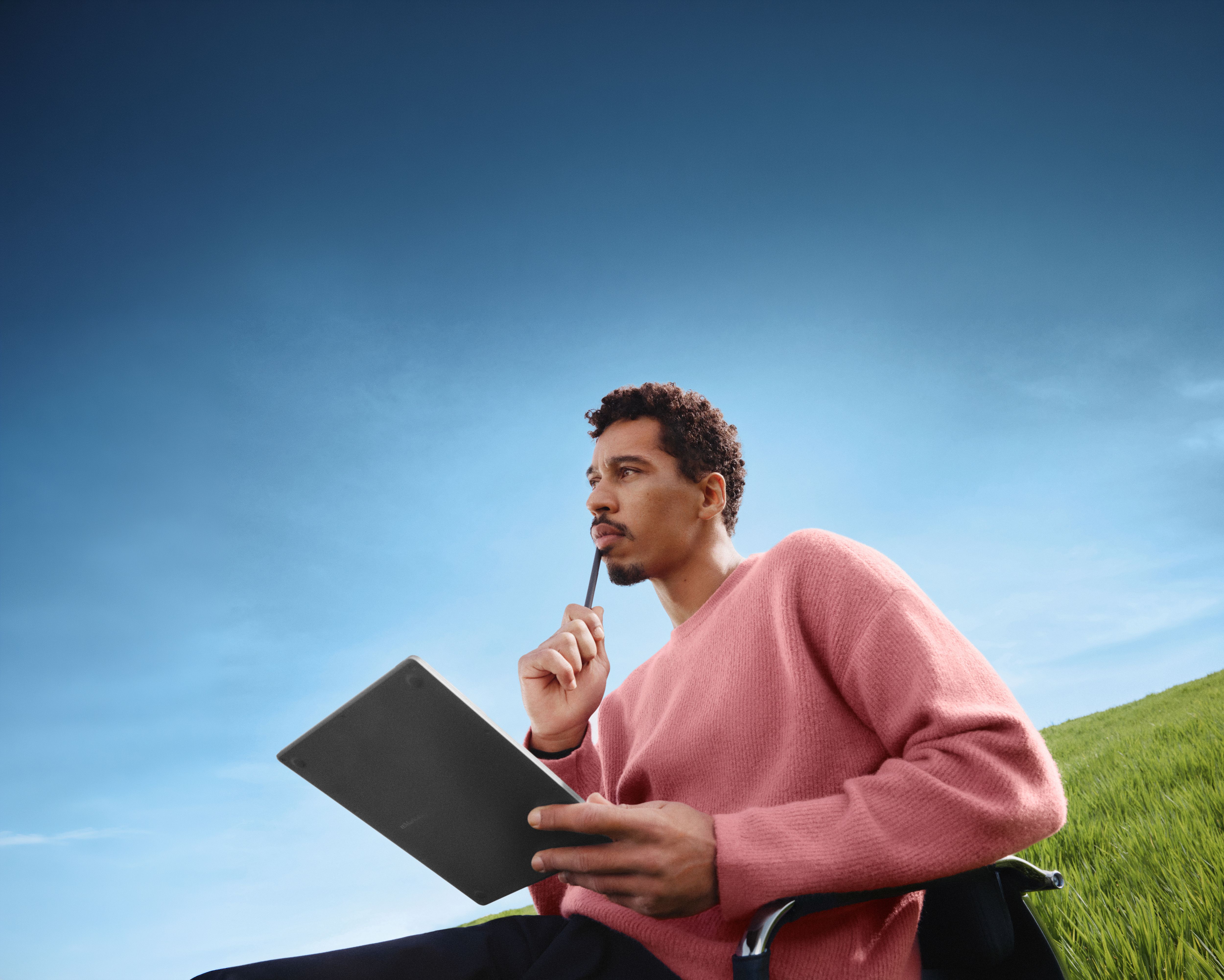 A man sitting on an office chair in a green field with blue sky, thinking with his reMarkable Paper Pure