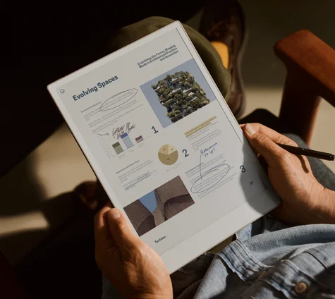 Person reviewing architecture document on a reMarkable Paper Pro tablet, using the Marker to take notes. The screen reads "Evolving Spaces".