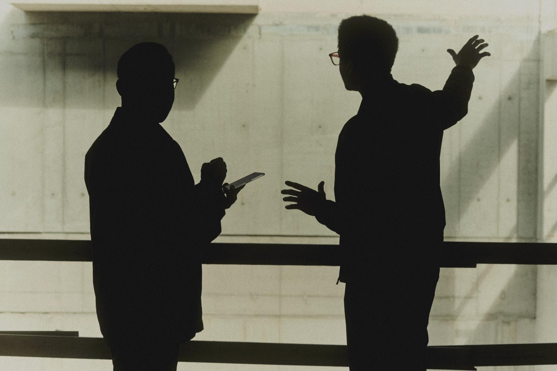 Two people silhouetted in discussion, one holding a reMarkable.
