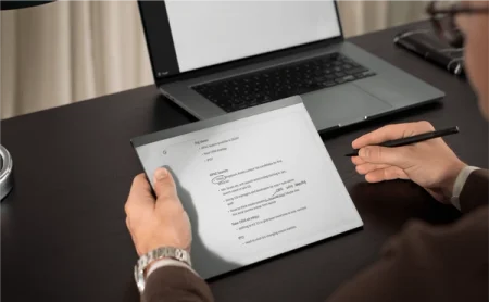 A reMarkable paper tablet displaying handwritten notes while a user writes with the Marker.