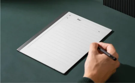 A reMarkable paper tablet displaying a dayplanner template page with lines and a hand writing a note with the Marker.
