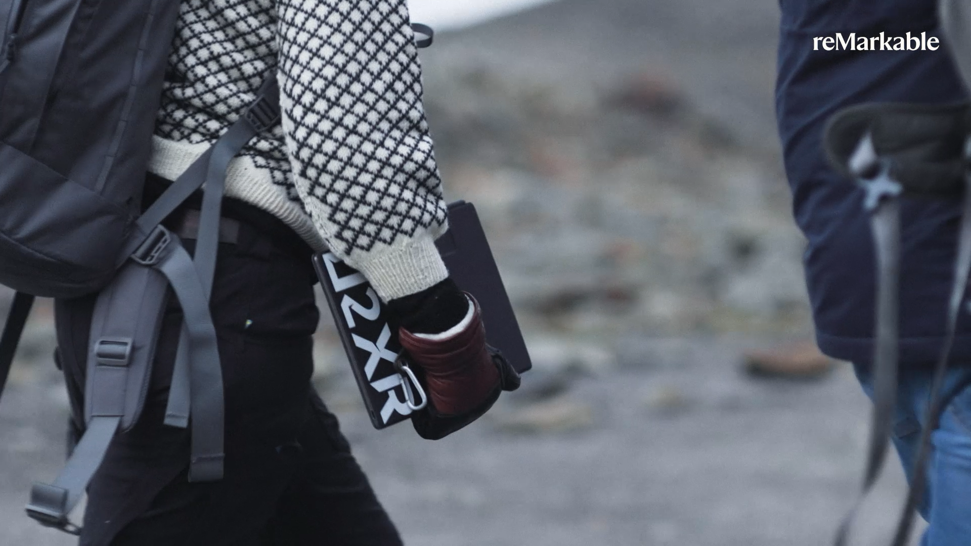 A reMarkable paper tablet being held by a person wearing a backpack.