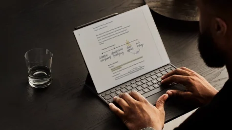 Typing on a reMarkable Paper Pro tablet with a Type Folio, next to a glass of water.