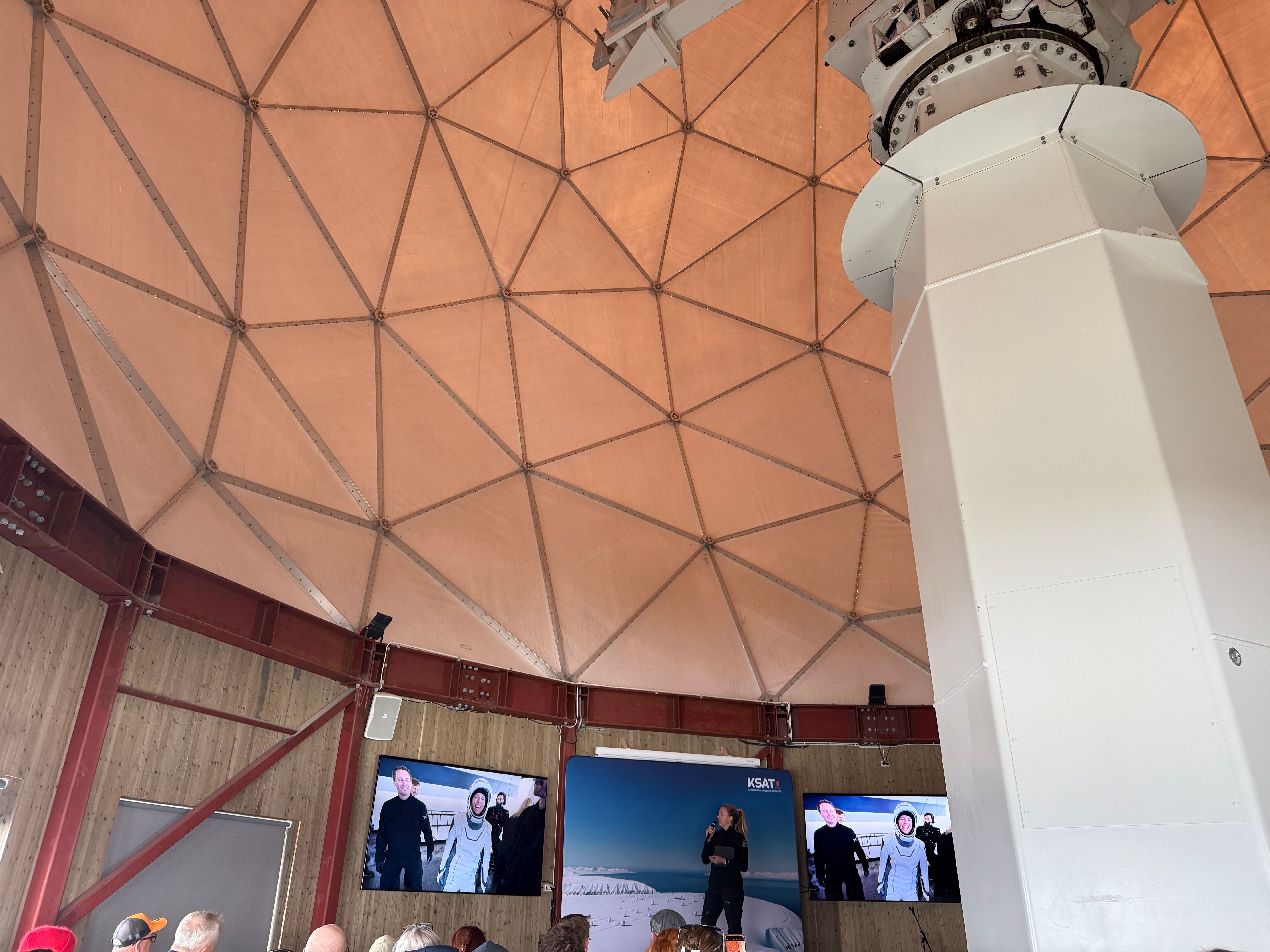 Jannicke Mikkelsen giving a speech on a stage in a large white structure under a geodesic dome with monitors displaying people.
